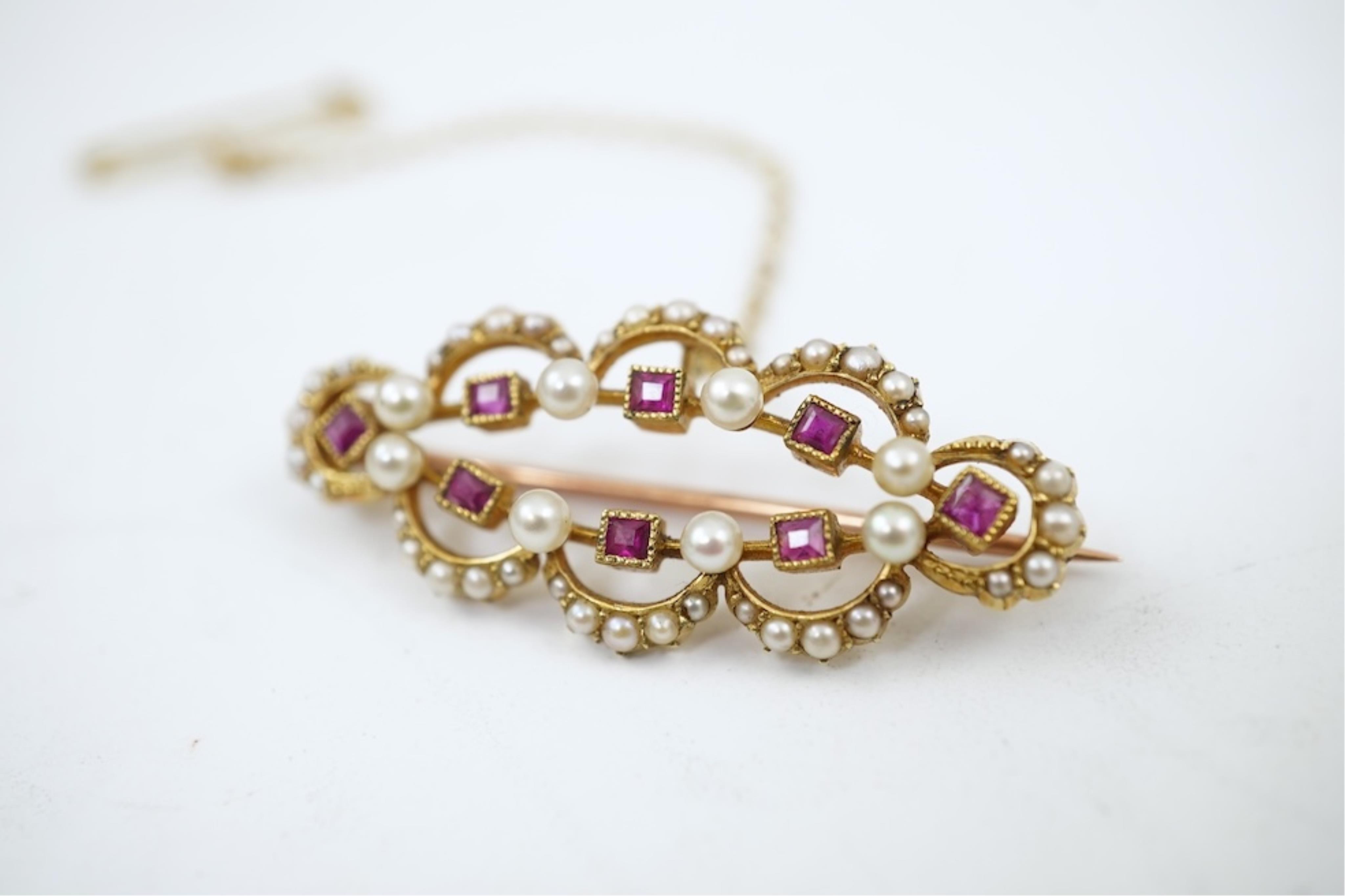 An Edwardian 15ct, ruby and seed pearl cluster set brooch, 33mm, with safety chain, gross weight 4.1 grams.